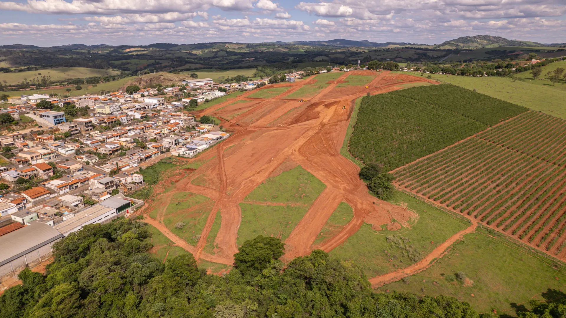 Aérea da terraplenagem do Ouro Verde, com o solo preparado para os lotes e a cidade de Cana Verde ao fundo